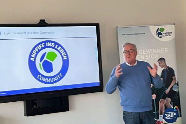 Mann pr&auml;sentiert das Logo der &bdquo;Anpfiff ins Leben Community&ldquo; auf einem Bildschirm in einem modernen Raum.