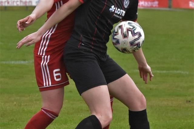 Zwei Fußballspielerinnen kämpfen um den Ball auf einem grünen Spielfeld, die eine in schwarzem, die andere in rotem Trikot.