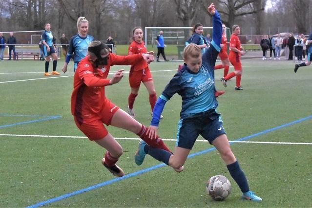 Zwei weibliche Fußballspielerinnen kämpfen um den Ball auf einem Kunstrasenfeld während eines Spiels.