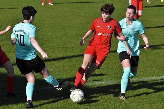 Drei Fu&szlig;ballspielerinnen k&auml;mpfen um den Ball auf einem gr&uuml;nen Rasenfeld w&auml;hrend eines Spiels.