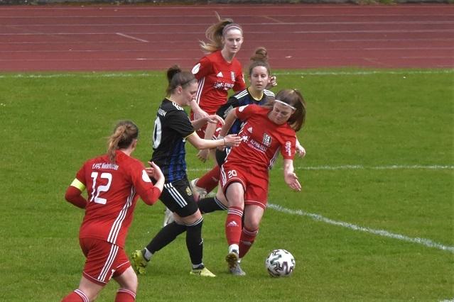 Zwei Fu&szlig;ballspielerinnen in roten Trikots k&auml;mpfen um den Ball, umgeben von weiteren Spielerinnen auf dem Spielfeld.