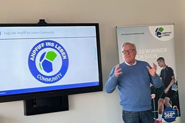 Mann pr&auml;sentiert das Logo der &bdquo;Anpfiff ins Leben Community&ldquo; auf einem Bildschirm in einem modernen Raum.
