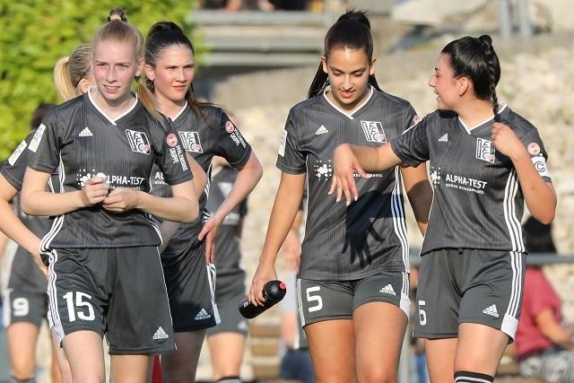 Fünf Fußballspielerinnen in grauen Trikots gehen gemeinsam auf dem Spielfeld, eine hält eine Wasserflasche in der Hand.