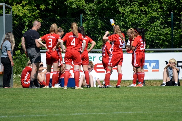 Sechs Fu&szlig;ballspielerinnen in roten Trikots stehen an der Seitenlinie, w&auml;hrend ein Trainer Anweisungen gibt.