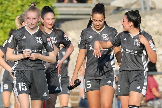 F&uuml;nf Fu&szlig;ballspielerinnen in grauen Trikots gehen gemeinsam auf dem Spielfeld, eine h&auml;lt eine Wasserflasche in der Hand.