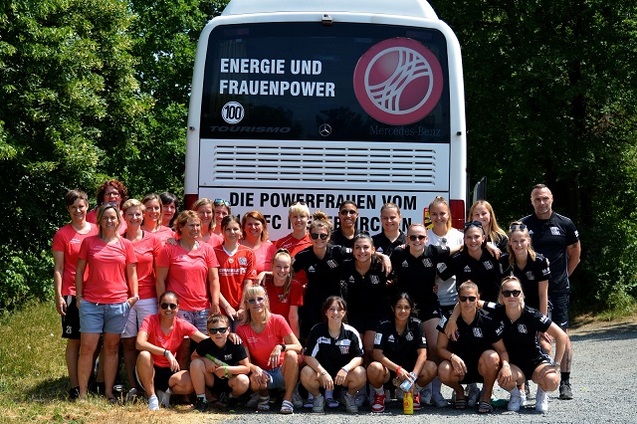 Gruppensfoto von Frauen in roten und schwarzen Trikots vor einem Bus mit der Aufschrift &bdquo;Energie und Frauenpower&ldquo;.