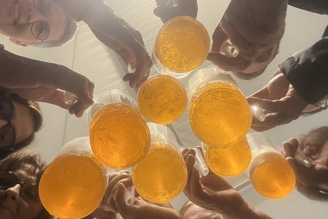 Ansicht von unten auf eine Gruppe von Personen, die Gl&auml;ser mit goldenem Getr&auml;nk zusammenhalten.