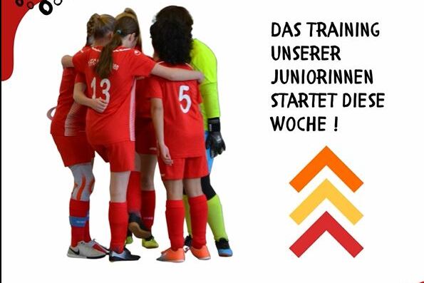 M&auml;dchenfu&szlig;ballmannschaft in roten Trikots versammelt sich, um das Training zu besprechen. Im Hintergrund ist eine Torh&uuml;terin zu sehen.