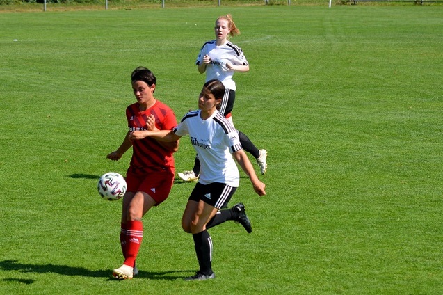 Drei Frauenfu&szlig;ballerinnen verfolgen einen Ball auf einem gr&uuml;nen Rasenplatz w&auml;hrend eines Spiels.