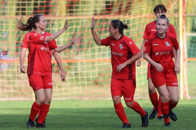 Vier Fu&szlig;ballspielerinnen in roten Trikots jubeln auf einem Rasenplatz vor dem Tor.
