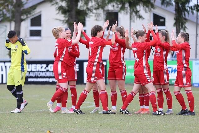 M&auml;dchenmannschaft in roten Trikots feiert mit Abklatschen auf einem Fu&szlig;ballfeld, Torh&uuml;terin im Hintergrund.