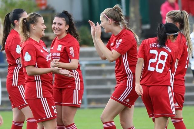F&uuml;nf Frauen in roten Fu&szlig;balltrikots feiern auf dem Spielfeld miteinander.