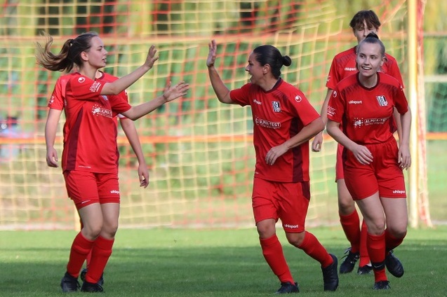 Vier Fu&szlig;ballspielerinnen in roten Trikots jubeln auf einem Rasenplatz vor dem Tor.