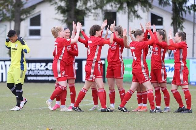 M&auml;dchenmannschaft in roten Trikots feiert mit Abklatschen auf einem Fu&szlig;ballfeld, Torh&uuml;terin im Hintergrund.