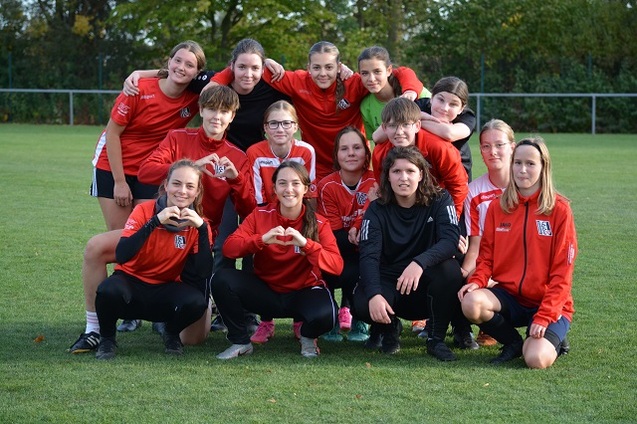 Gruppenfoto einer Fu&szlig;ballmannschaft von 14 M&auml;dchen in roten Trikots, auf einem Rasenfeld, l&auml;chelnd und posierend.