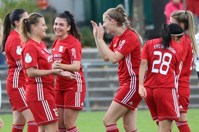 F&uuml;nf Frauen in roten Fu&szlig;balltrikots feiern auf dem Spielfeld miteinander.