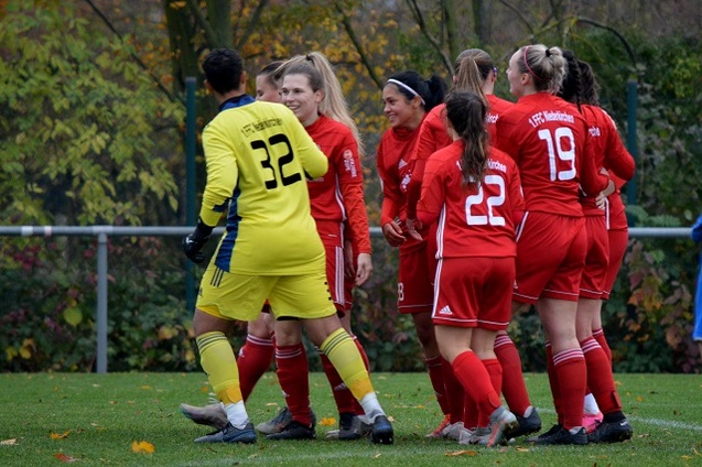 Gruppenbild von Fu&szlig;ballspielerinnen in roten Trikots, die mit einer Torh&uuml;terin in gelbem Trikot jubeln.