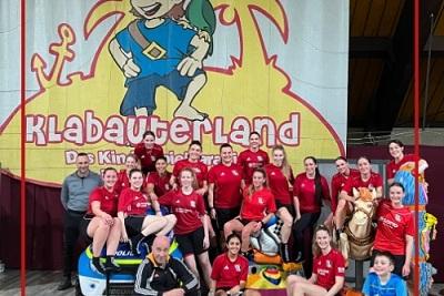 Gruppe von Sportlerinnen in roten Trikots posiert vor einem bunten Wandgem&auml;lde im Klabauterland.