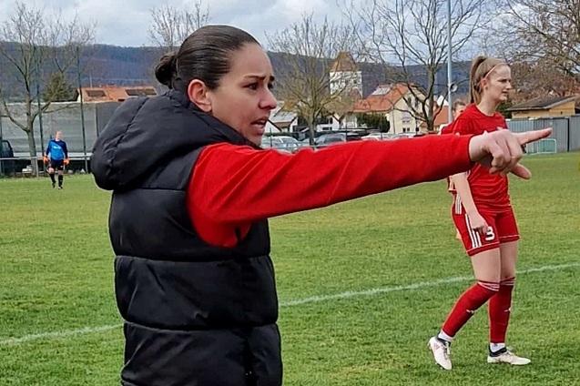 Trainerin in roter Jacke gibt Anweisungen am Fu&szlig;ballfeld, w&auml;hrend eine Spielerin im Hintergrund steht.