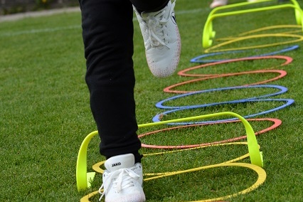 Ein Spieler springt &uuml;ber mehrere bunte H&uuml;rden auf einem Rasenplatz w&auml;hrend eines Trainings.