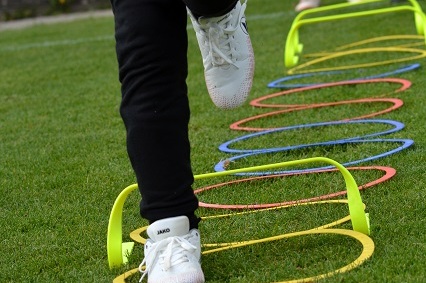 Ein Spieler springt &uuml;ber mehrere bunte H&uuml;rden auf einem Rasenplatz w&auml;hrend eines Trainings.
