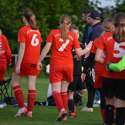 Gruppe von M&auml;dchenfu&szlig;ballerinnen in roten Trikots beim Verlassen des Spielfelds, Trainer beobachtet sie.