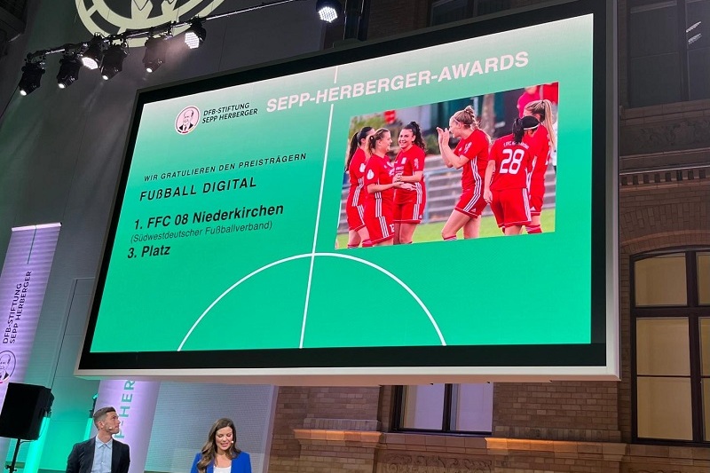 B&uuml;hne bei den Sepp-Herberger-Awards mit Pr&auml;sentation der Preistr&auml;ger und einer Frau in blauer Kleidung, die anspricht.