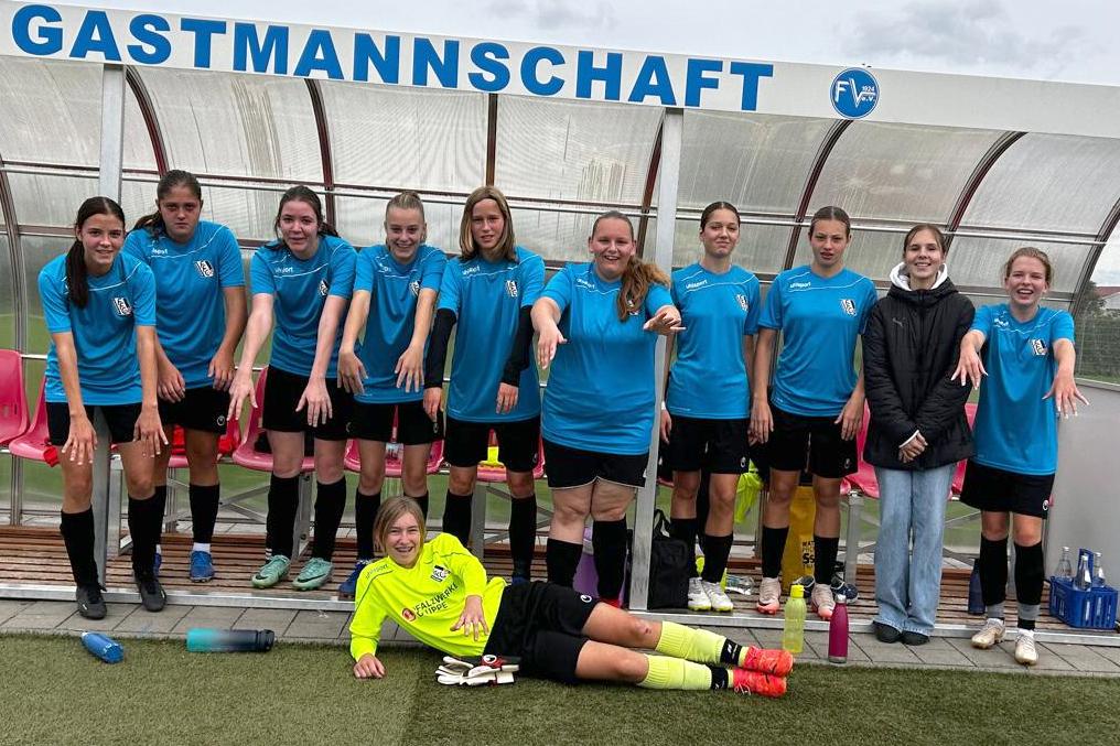 Mannschaftsfoto einer Fußball-Damenmannschaft in azulfarbenen Trikots, posierend auf einer Bank neben dem Spielfeld.
