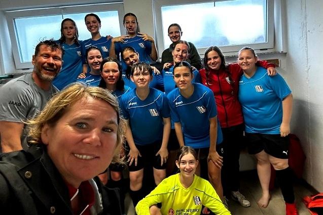 Gruppe von Fu&szlig;ballspielerinnen in blauen Trikots, mit Trainer, in Umkleideraum nach dem Training.