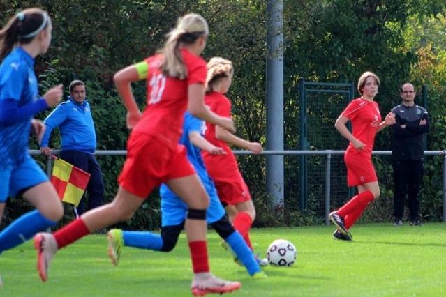 Spielszene mit mehreren Mädchen in roten Trikots, die auf einem Fußballfeld laufen, während ein Trainer zuschaut.