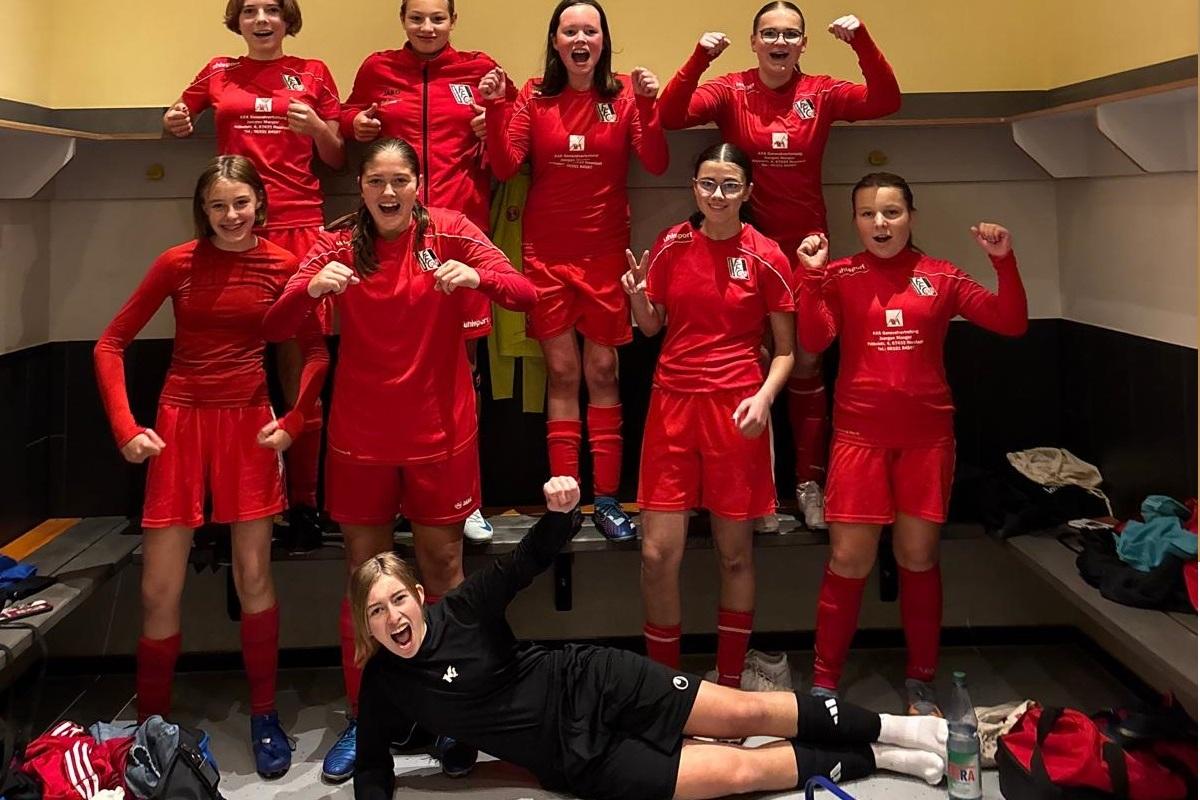 Gruppe von M&auml;dchen im roten Fu&szlig;balltrikot posiert fr&ouml;hlich in einer Kabine, einige heben die Arme zum Jubel.