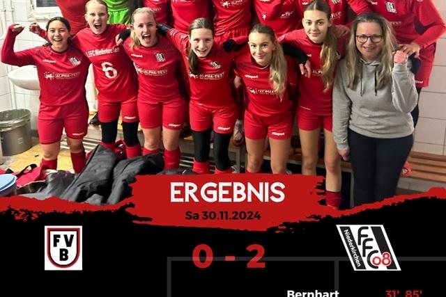 Gruppe von Frauenfu&szlig;ballspielerinnen in roten Trikots feiert in Umkleidekabine. Anzeigetafel zeigt Ergebnis: 0-2.