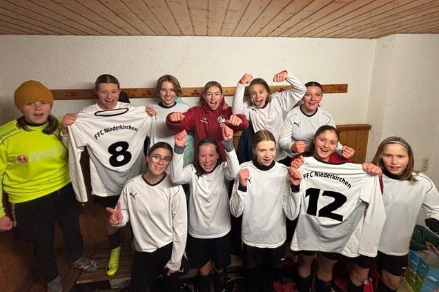 M&auml;dchenfu&szlig;ballmannschaft zeigt jubelnd ihre Trikots des FFC Niederkirchen in einem Umkleideraum.