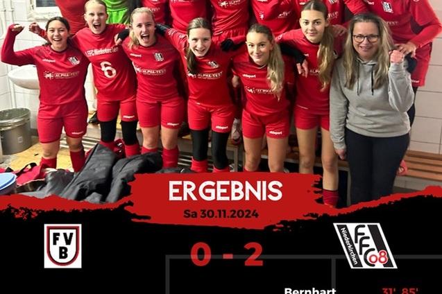 Gruppe von Frauenfu&szlig;ballspielerinnen in roten Trikots feiert in Umkleidekabine. Anzeigetafel zeigt Ergebnis: 0-2.