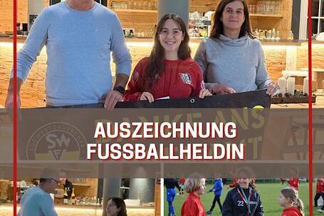 Drei Personen stehen vor einer Theke und halten ein Banner mit der Aufschrift &bdquo;Auszeichnung Fussballheldin&ldquo;.