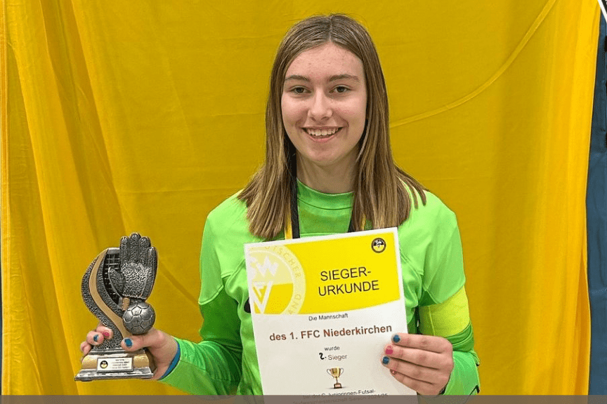 Sophia Görh hält eine Siegerurkunde und eine Trophäe in einer Sporthalle, hinter ihr blauer und gelber Hintergrund.