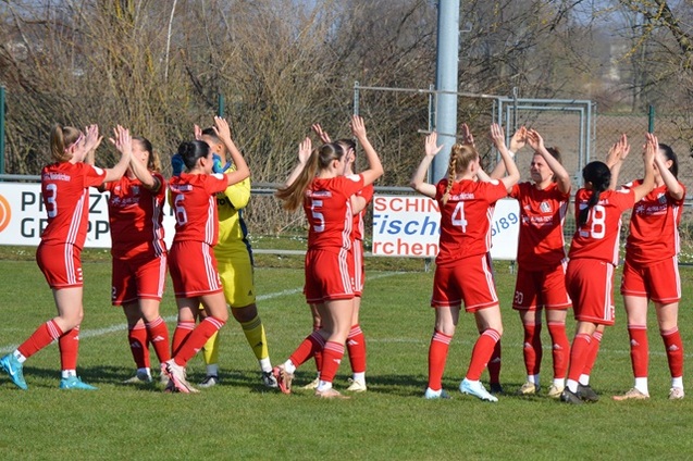 Eine Gruppe von Fu&szlig;ballspielerinnen in roten Trikots applaudiert auf einem Rasenplatz nach einem Spiel.