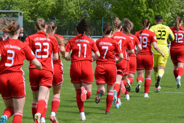 Mannschaft des 1. FFC Niederkirchen in roten Trikots, sprintend auf einem Rasenplatz w&auml;hrend eines Spiels.