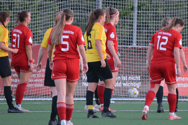 Spielszene mit Spielerinnen in roten Trikots gegen gelbe Trikots, Ergebnisanzeige 2-3, Fu&szlig;ballfeld im Hintergrund.