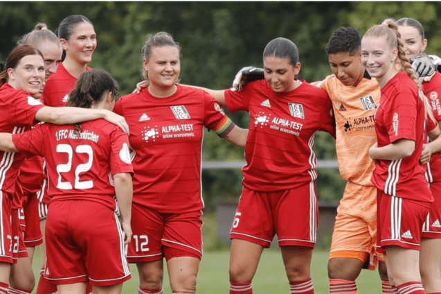 Gruppenumarmung von Spielerinnen in roten Trikots nach einem Fu&szlig;ballspiel, mit Ergebnis 1-5 im Hintergrund.