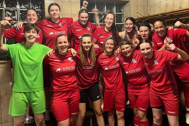 Gruppenselfie von weiblichen Fu&szlig;ballspielerinnen in roten Trikots, die fr&ouml;hlich im Umkleideraum posieren.