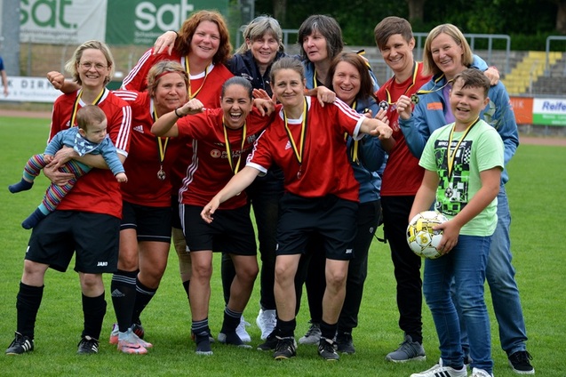 Gruppenszene von Frauenfu&szlig;ballspielerinnen in roten Trikots, die mit Medaillen und einem Ball auf einem Sportplatz posieren.