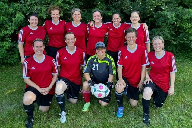 Gruppenfoto einer Fu&szlig;ballmannschaft mit elf Frauen in roten Trikots, stehend und kniend auf einer Wiese.