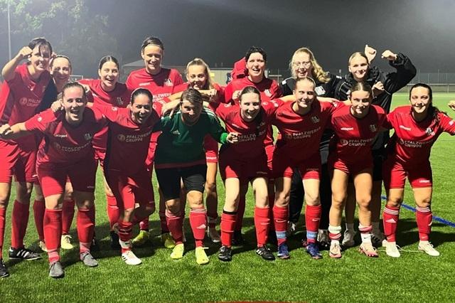 Gruppe von Fußballspielerinnen in roten Trikots feiert nach einem Spiel auf einem Kunstrasenplatz.