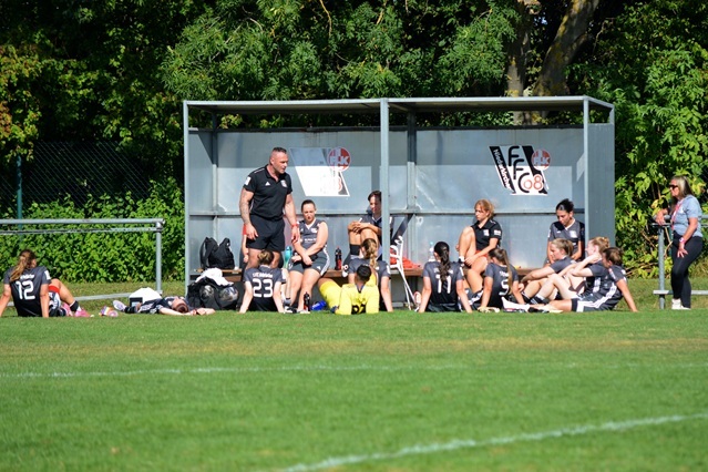 Trainerbesprechung mit einer Gruppe von M&auml;dchenmannschaft auf der Ersatzbank w&auml;hrend eines Fu&szlig;ballspiels im Freien.
