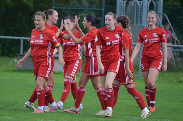 Gruppe von Fu&szlig;ballspielerinnen in roten Trikots feiert gemeinsam auf dem Spielfeld.