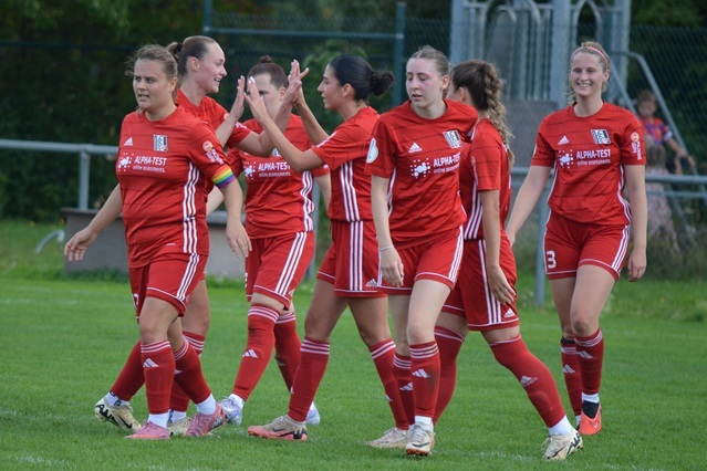 Gruppe von Fu&szlig;ballspielerinnen in roten Trikots feiert gemeinsam auf dem Spielfeld.