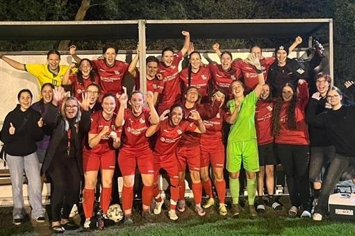 Gruppe von Fußballspielerinnen in roten Trikots feiert jubelnd nach dem Spiel, umgeben von Unterstützern.