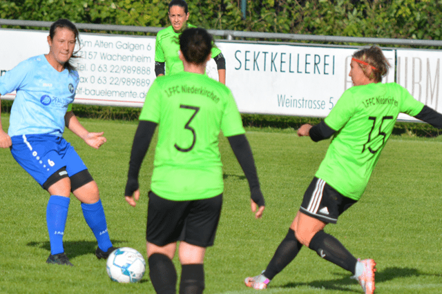 Vereinsfu&szlig;ballspiel: Spielerinnen in gr&uuml;nen Trikots, Gegnerin im blauen Trikot, Ball auf einem Rasenspielfeld.