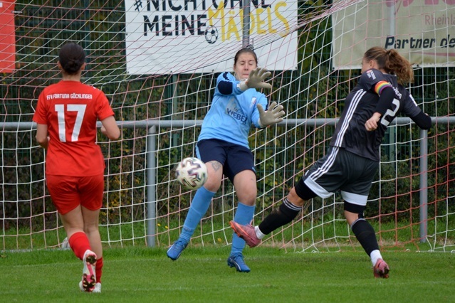 Torwartin f&auml;ngt einen Ball, w&auml;hrend zwei Spielerinnen auf dem Feld in rot und schwarz positioniert sind.